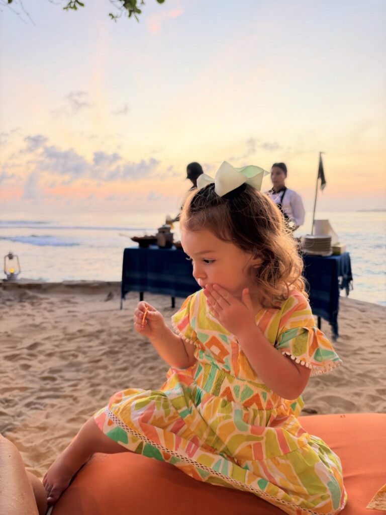 Toddler on the beach at sunset beside a beach dinner setup at NIHI Sumba