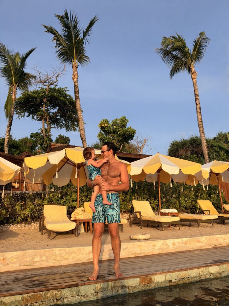Father holding his toddler daughter by the pool and beach umbrellas at NIHI Sumba