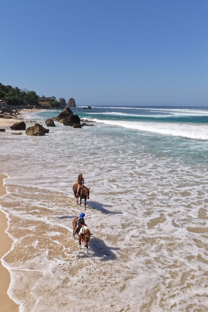 Drone view of Christina and her son horseback riding in the surf at NIHI Sumba